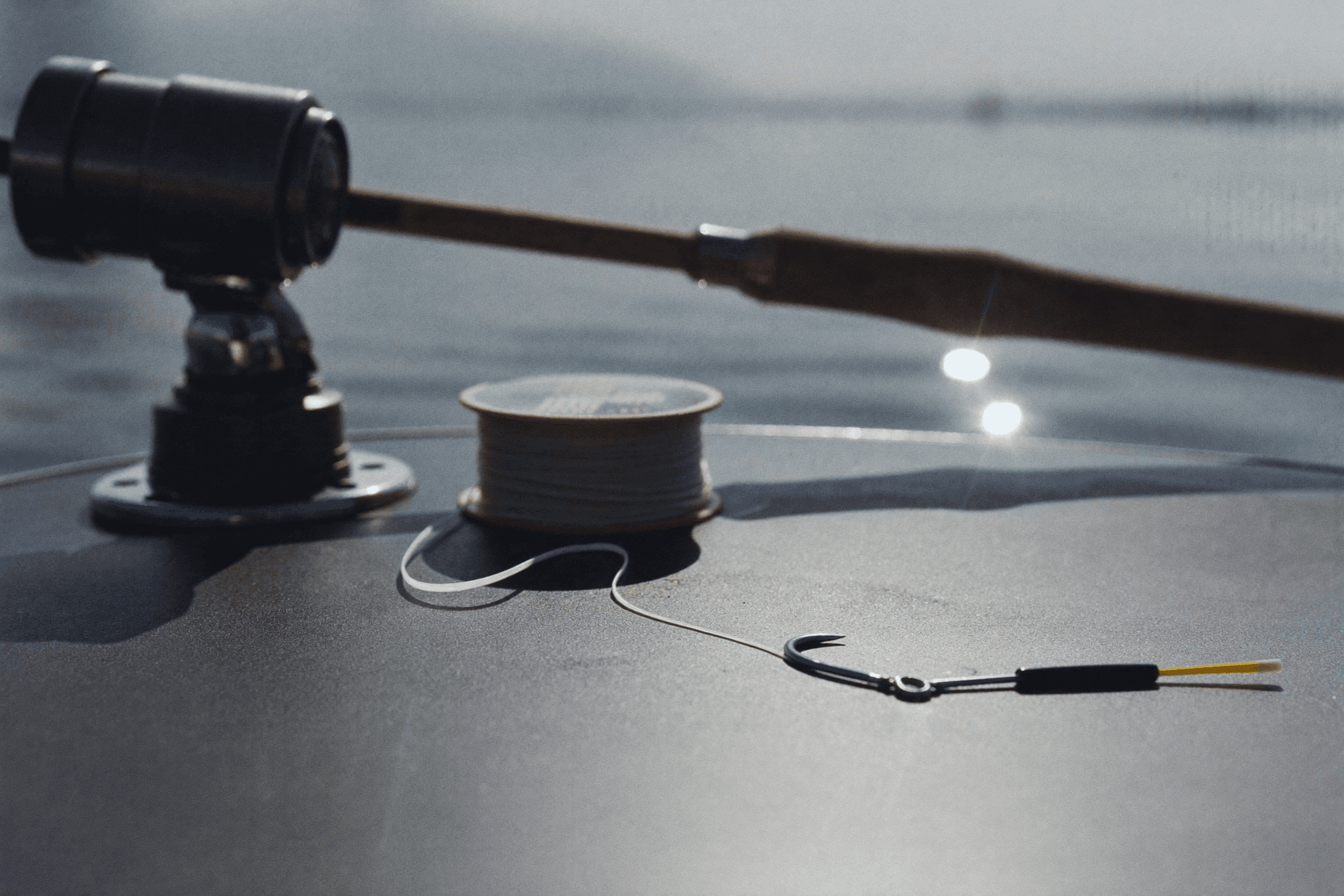 Drop shot rig on a boat gunwale at dawn: hook with soft plastic, long tag line and cylinder weight beside a spinning rod.