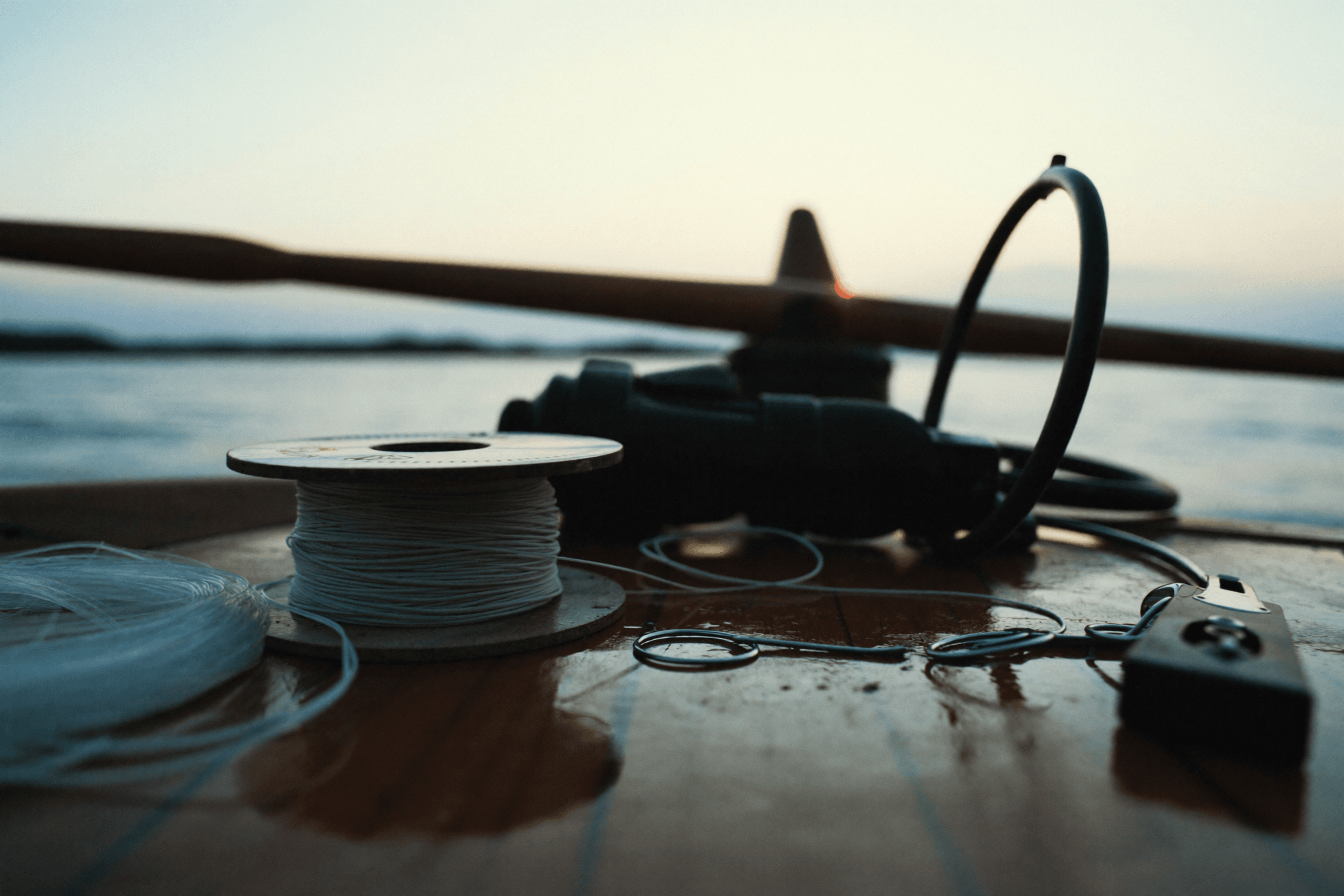 Spool of braided line, clear leader, line nippers and two hooks laid on a damp wooden gunwale at dawn.
