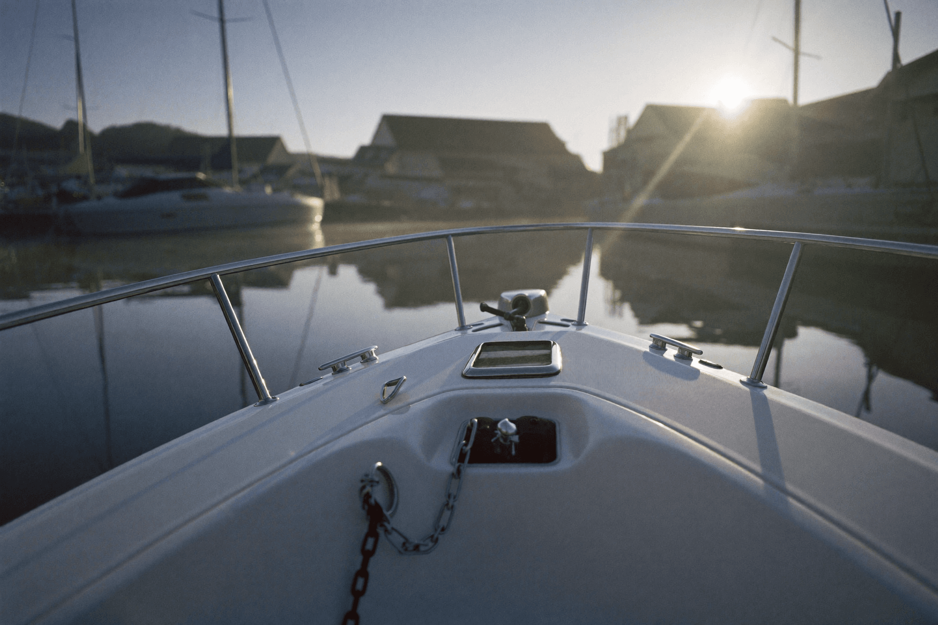 Bow of a white motorboat on calm water at dawn, showing the stem, bow rail, anchor in its roller and a deck cleat.